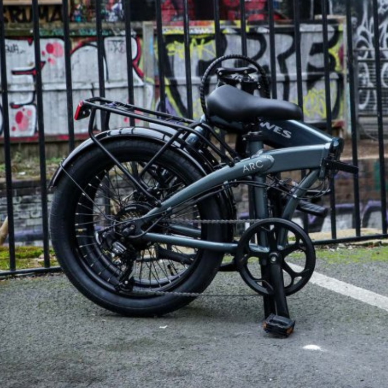 Dawes Arc, electric folding bike, folded by a railing with graffiti on wall behind