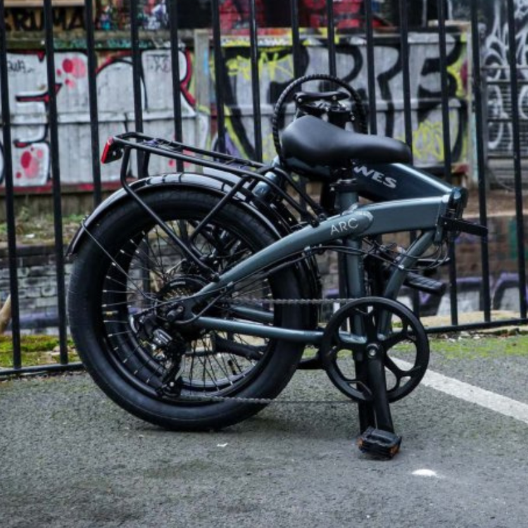 Dawes Arc, electric folding bike, folded by a railing with graffiti on wall behind