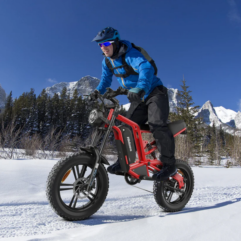 Man in blue jacket riding Hidoes B6 Cruiser in the snow with snow covered mountains in background