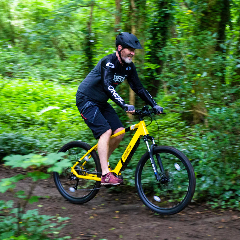 White bearded man in black riding yellow Mark 2 Scrambler through forest