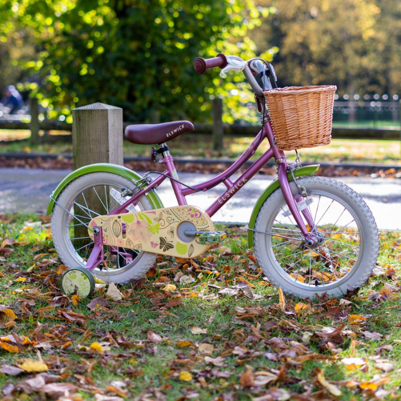 Pink Elswick Hope children's bike with a basket on a grassy area with leaves