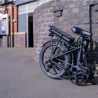 Black folding FALCON BREEZE e-bik leaning against a brick wall outdoors by train station