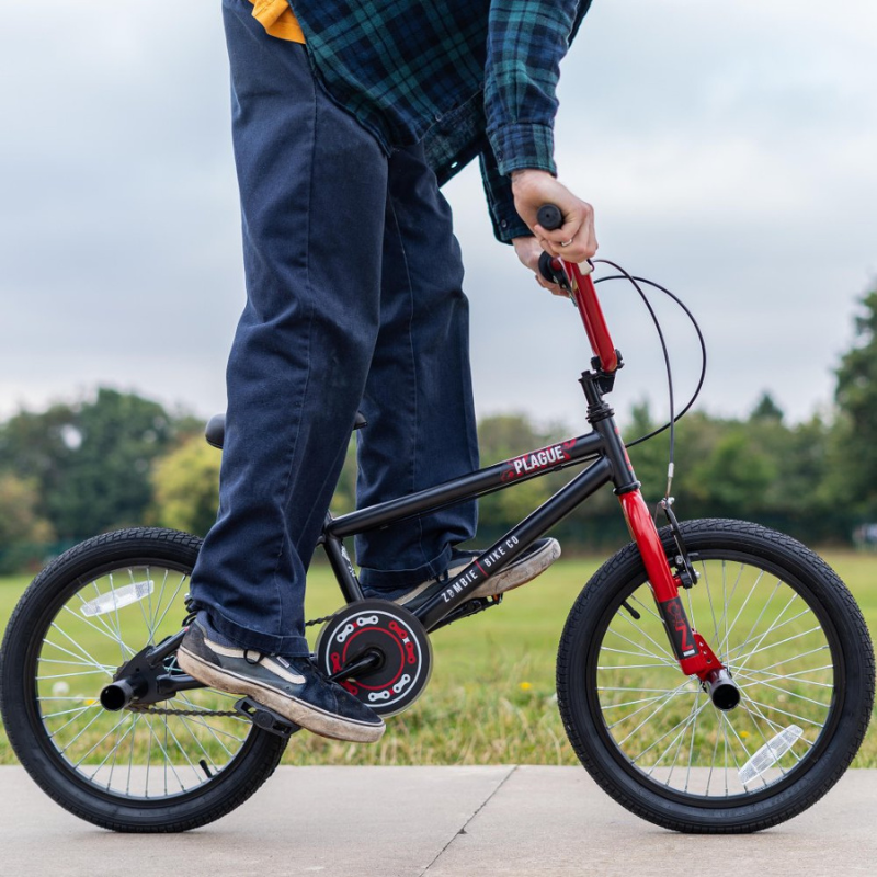 Person standing on a black and red Zombie Plague bmx in an outdoor setting with trees and grass.