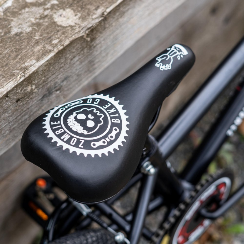 Bicycle seat with a Zombie Bike Co logo leaning on a wooden fence