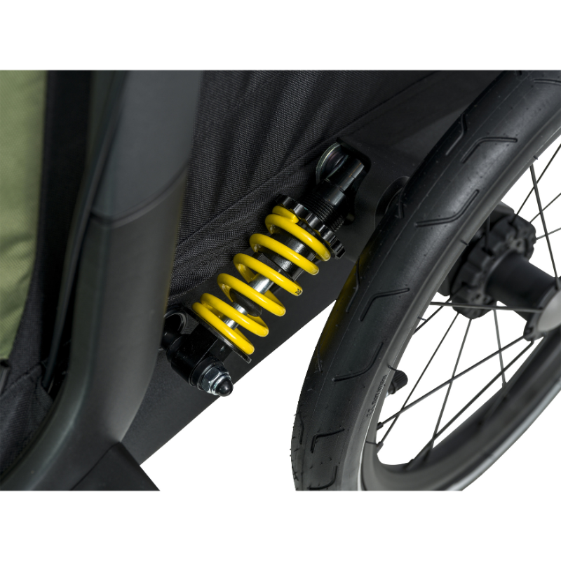 Close-up of a prominent bright yellow rear shock absorber spring on a black and olive hamax stroller, set against a clean white background.