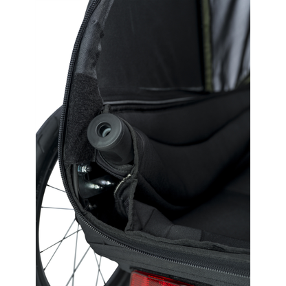 Close-up of a black bicycle trailer or storage bag interior with a zipper opening, showing a folded black component stored inside and part of a wheel visible at the edge.