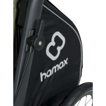 Close-up of a strollerpark brake lever and canopy in black with a white Hamax logo and brand name, attached to a dark stroller frame.