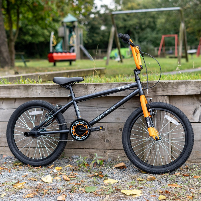 Black and orange bicycle leaning against a wooden fence with a playground in the background